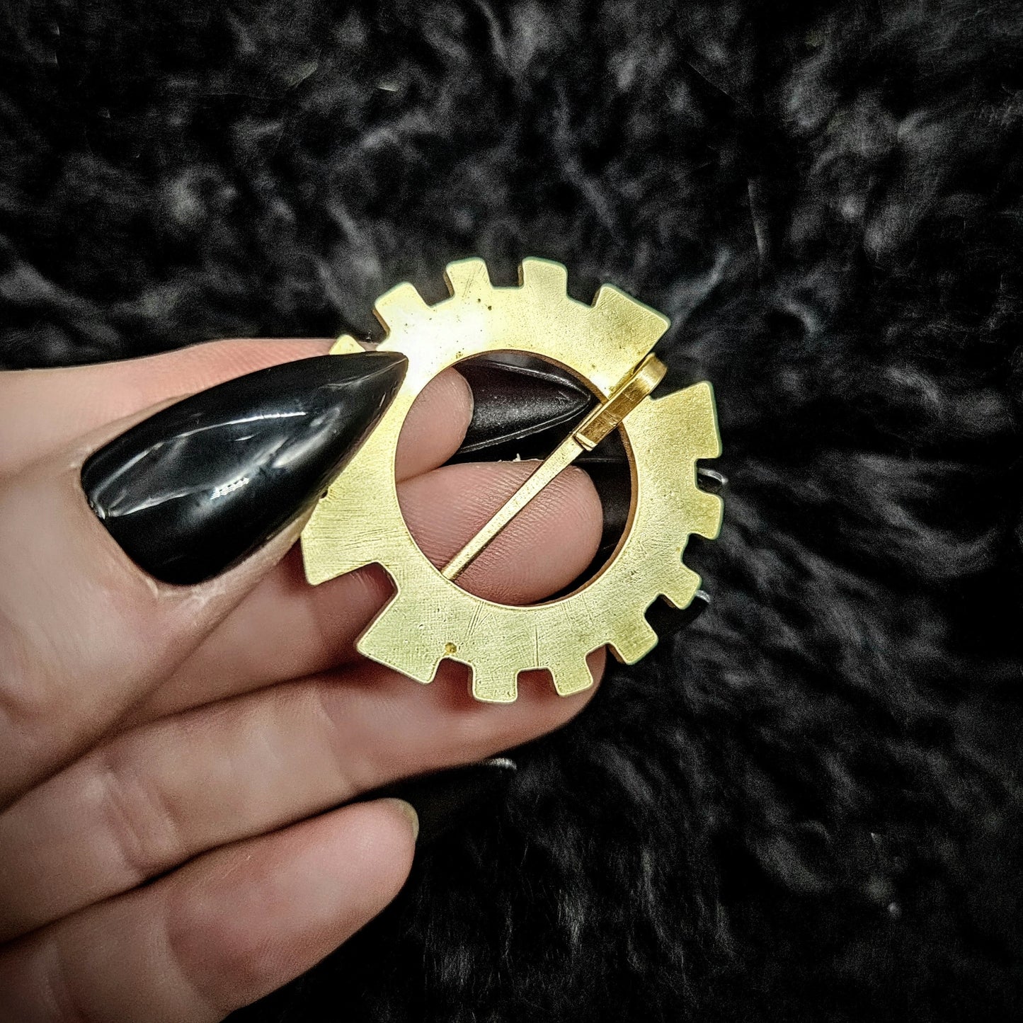 Gold gear-shaped brooch w held by a hand on a dark textured background