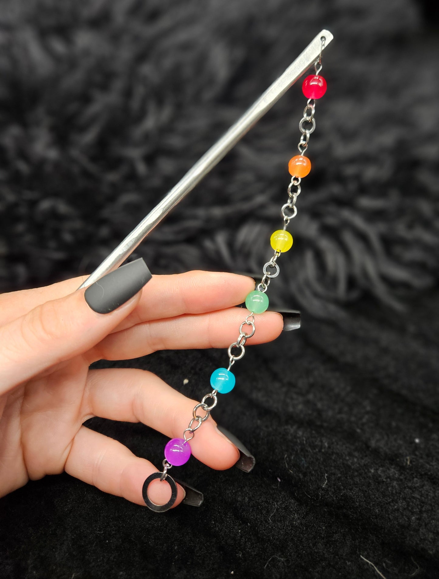 Hand holding a metal hairstick with colorful beads on a dark textured background