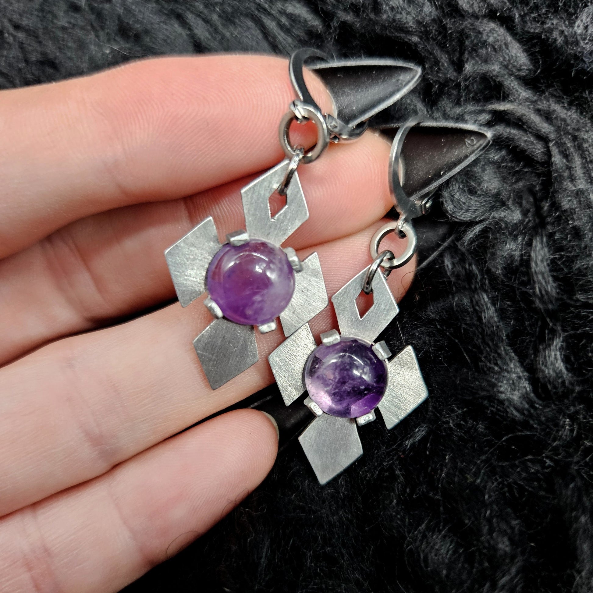 Silver earrings with purple gemstones held by a hand on a dark textured background