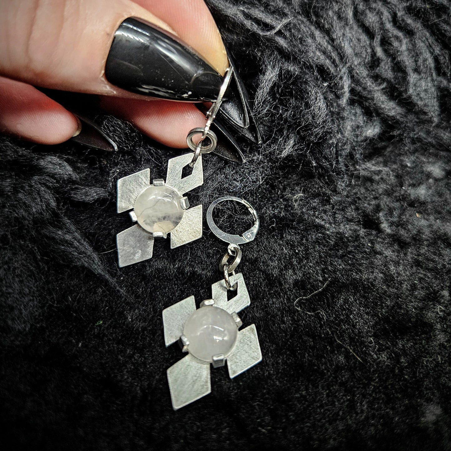 Silver earrings with stone set in a star shape design held by a hand against a textured black background