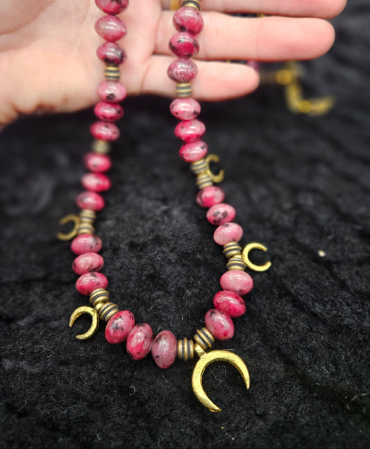 Pink beaded necklace with gold accents held by a hand against a dark textured background