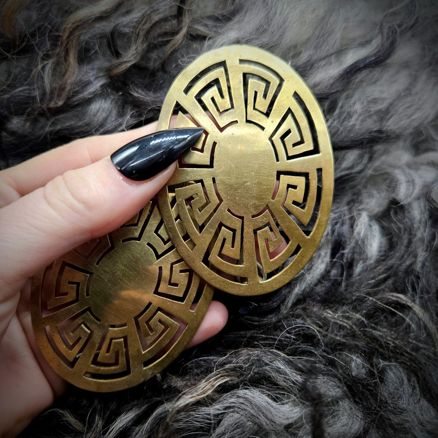 Gold oval turtle broach with intricate patterns held by a hand against a textured gray background
