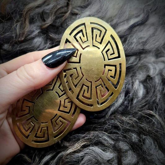 Gold oval turtle broach with intricate patterns held by a hand against a textured gray background