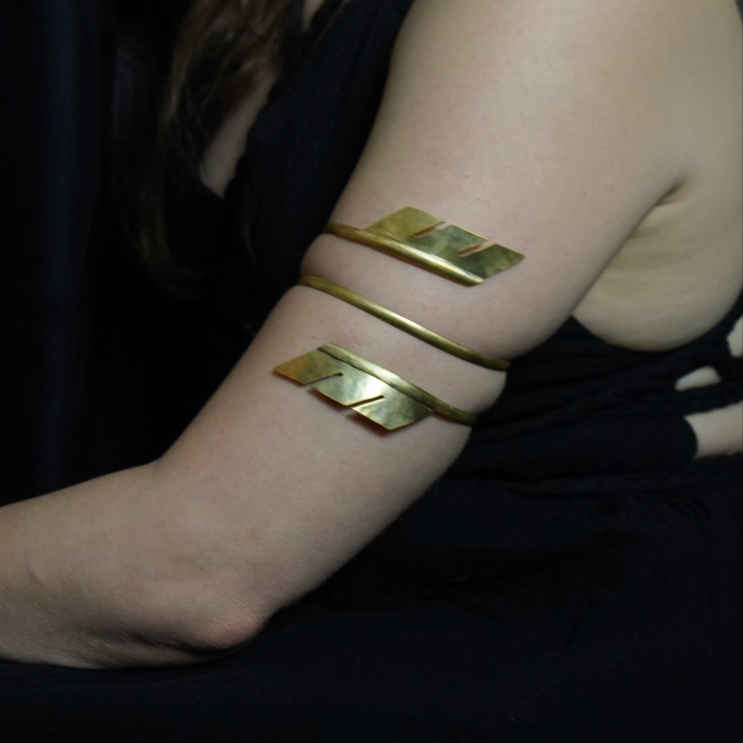 Woman wearing gold arm bands against a dark background