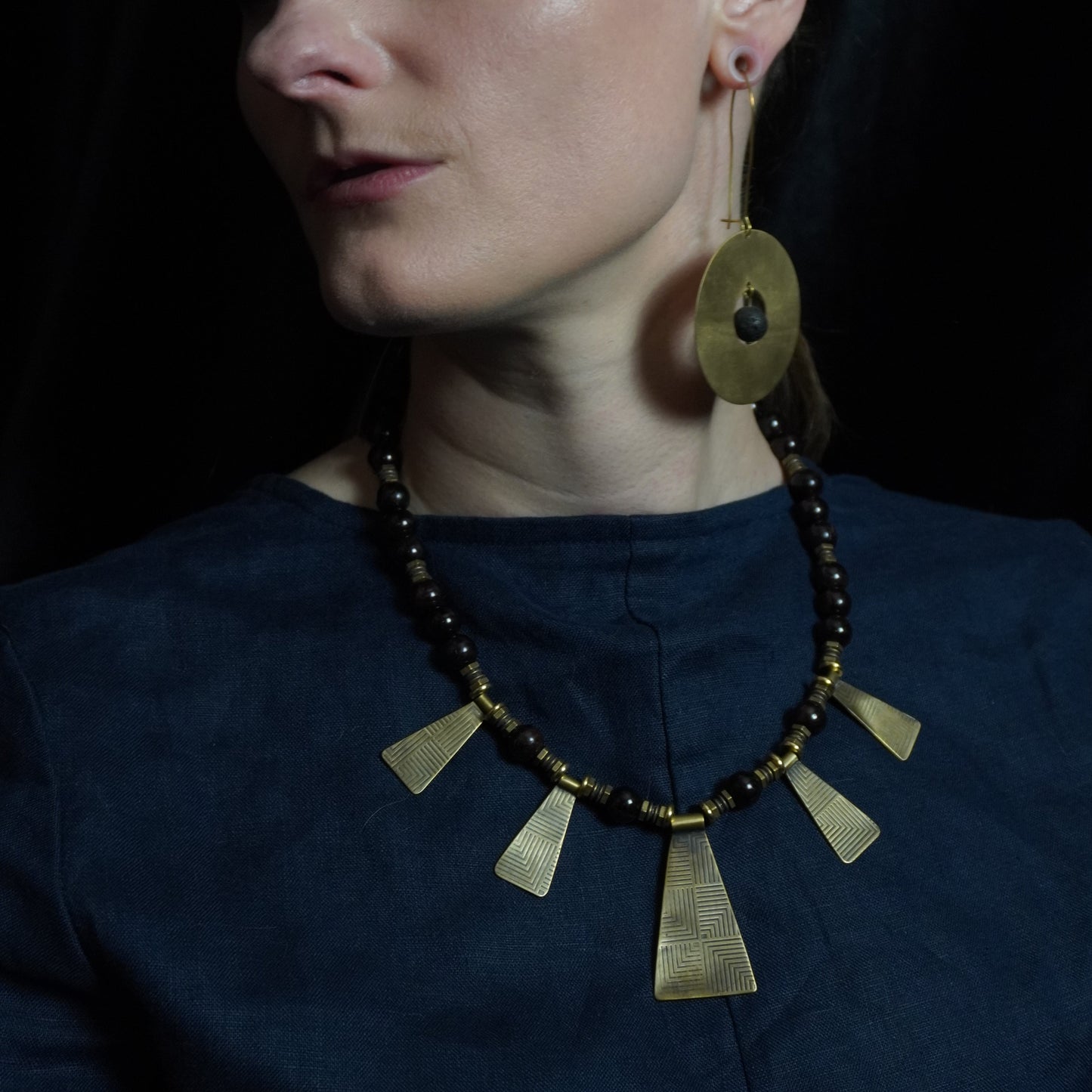Person wearing a dark blue garment with a decorative necklace against a dark background